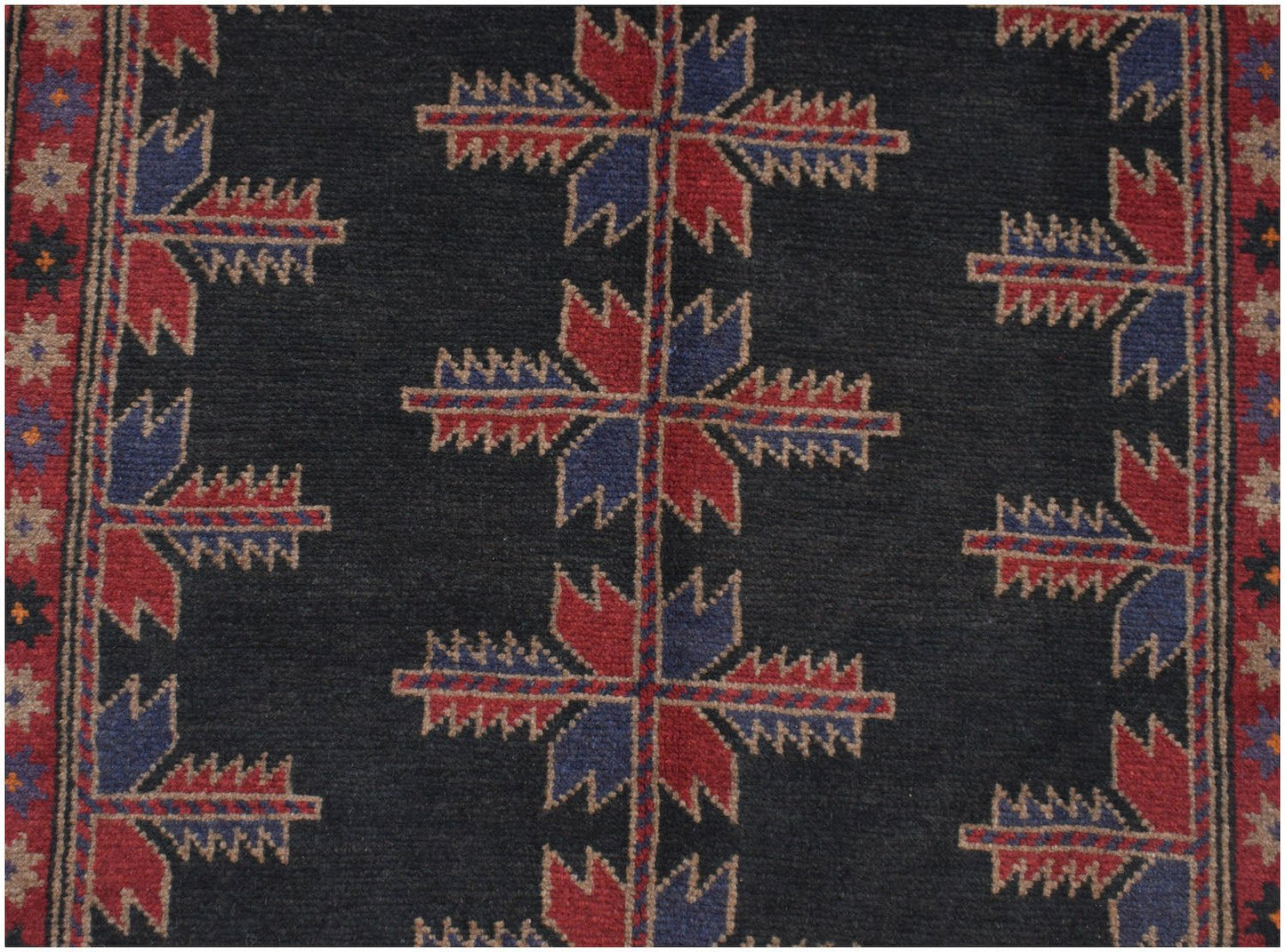 Handmade Afghan Baluch rug featuring a dark field with repeating geometric floral motifs.