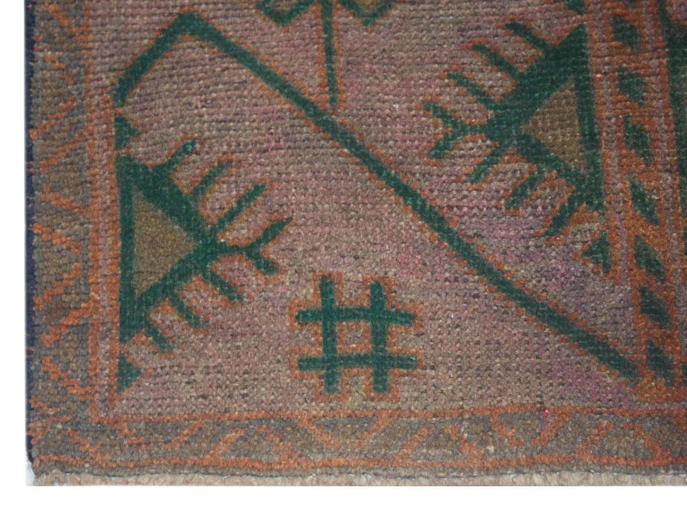 A handmade Afghan Baluch rug featuring a geometric green and brown pattern on a muted pink field.