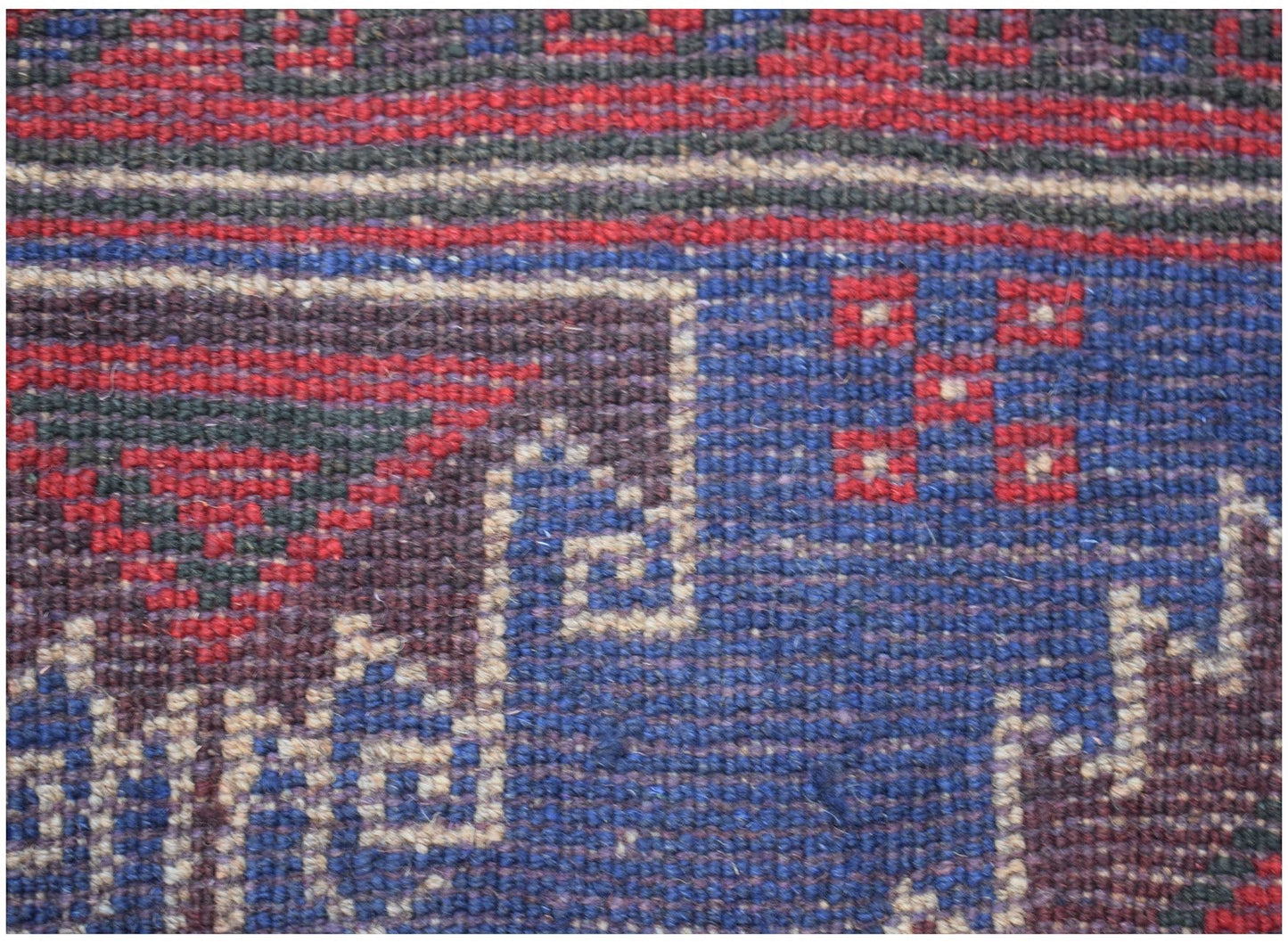 A close-up of a handmade Afghan Baluch rug featuring geometric patterns in red, blue, and ivory.
