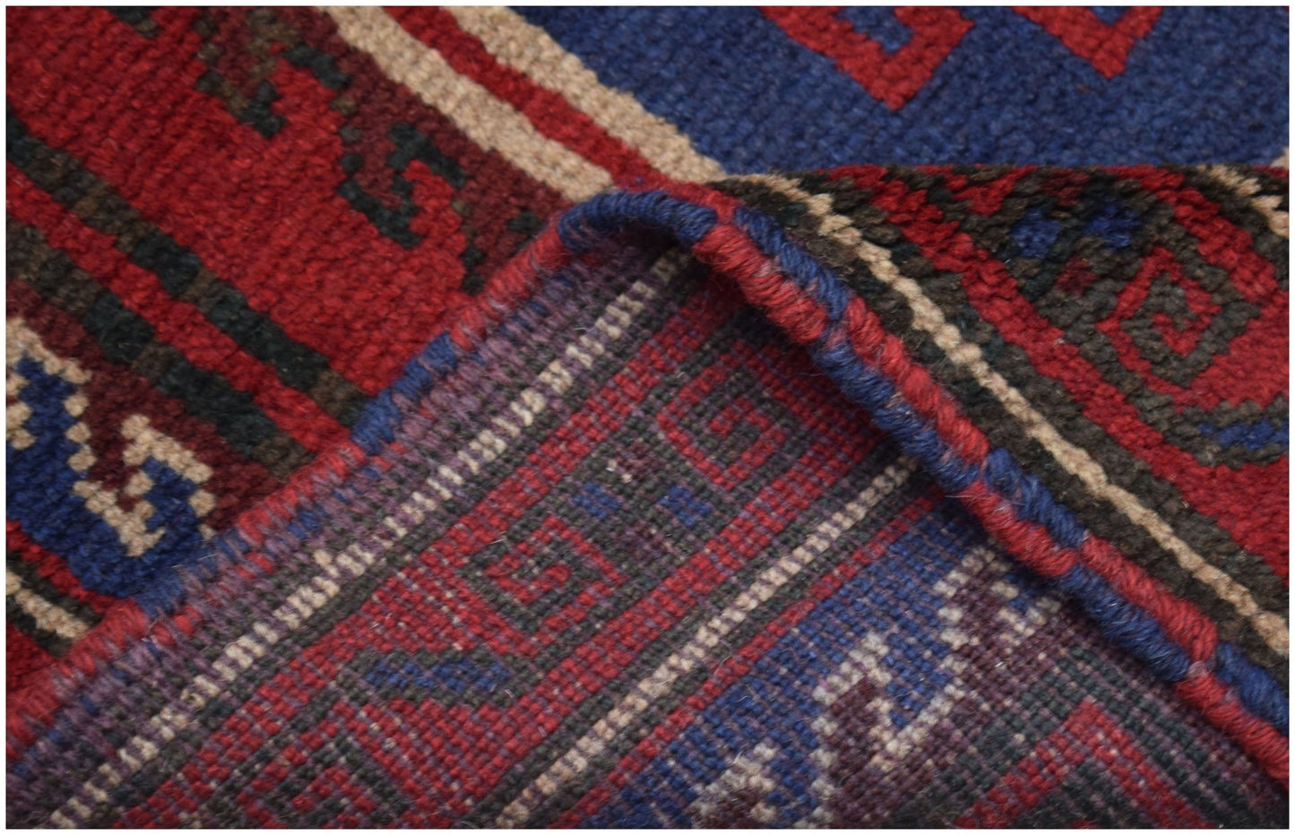 A close-up view of a handmade Afghan Baluch rug featuring geometric patterns in red, blue, and brown.