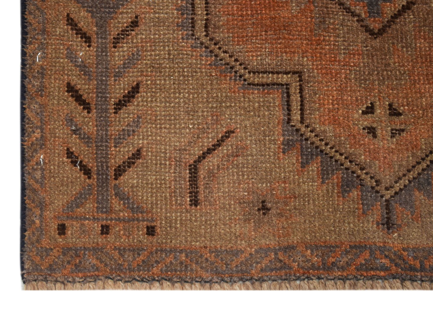A close-up of an Afghan Baluch rug featuring geometric patterns in shades of brown and orange.