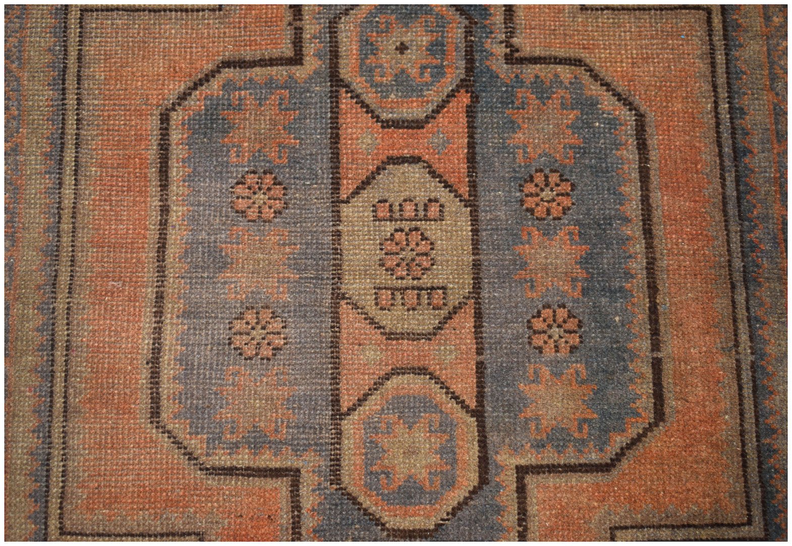 Handmade Afghan Baluch rug featuring geometric floral motifs in shades of orange and blue.