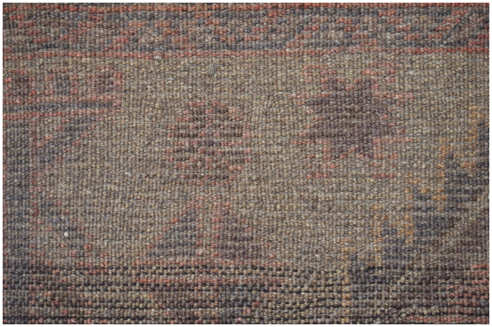 A close-up of a handmade Afghan Baluch wool rug featuring geometric patterns in earthy tones.