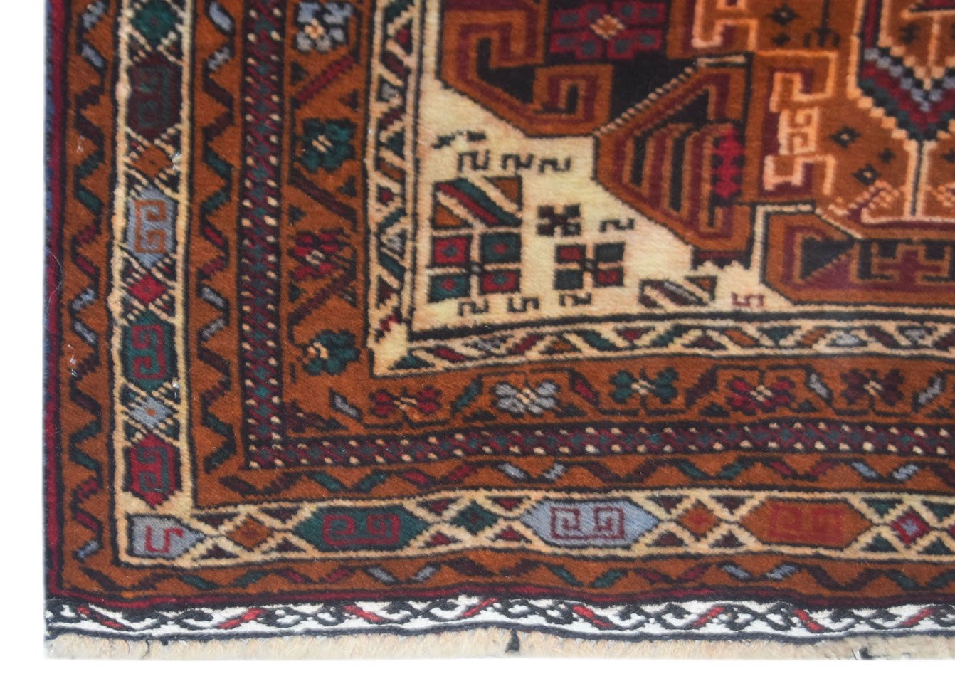 A corner view of a handmade vintage Afghan Baluch rug featuring geometric patterns in rust, cream, and blue.