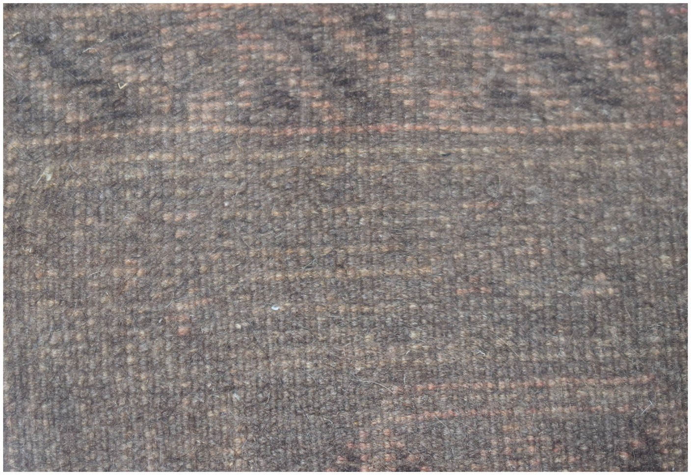 A close-up view of a handmade Afghan Baluch wool rug featuring a dark, textured geometric pattern.