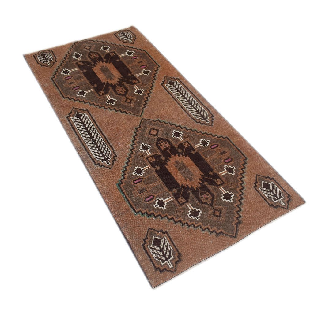 A handmade Afghan Baluch rug featuring two dark geometric medallions on a brown field.