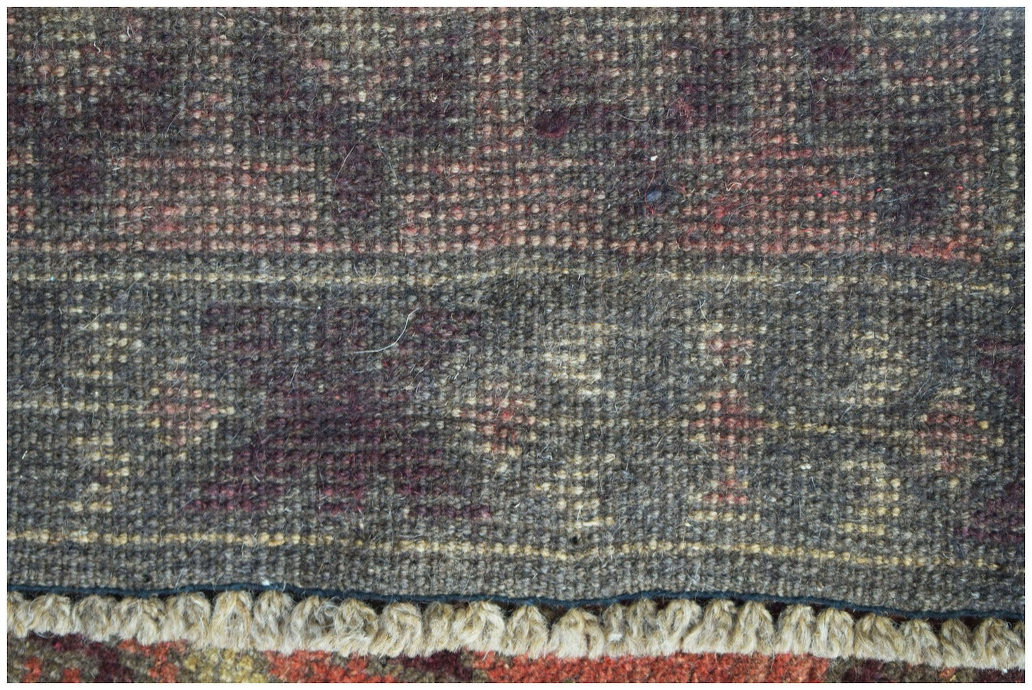 A close-up of a handmade Afghan Baluch rug featuring dark wool patterns and a fringed edge.