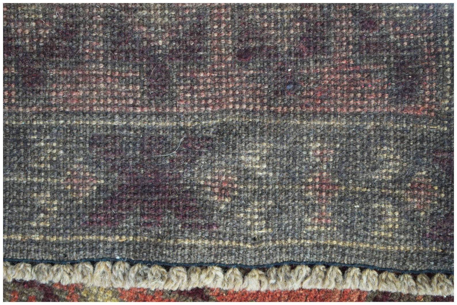 A close-up of a handmade Afghan Baluch rug featuring dark wool patterns and a fringed edge.