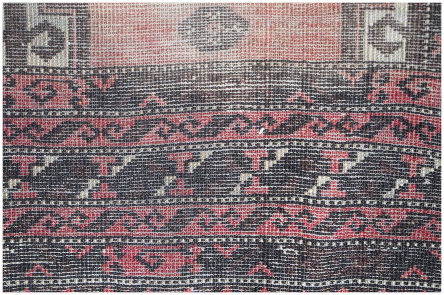 A close-up of a vintage Afghan Baluch rug featuring intricate geometric patterns in red and black.