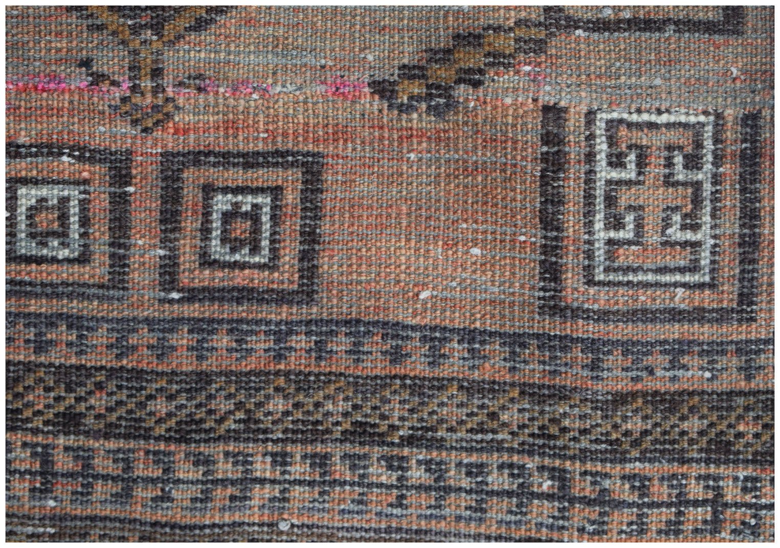 A close-up of a handmade Afghan Baluch rug featuring geometric patterns in orange and dark brown.