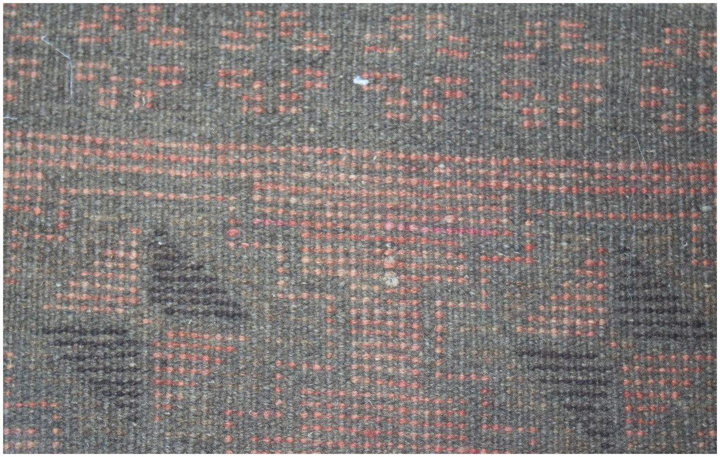 A close-up of a handmade Afghan Baluch rug featuring geometric patterns in brown and orange wool.