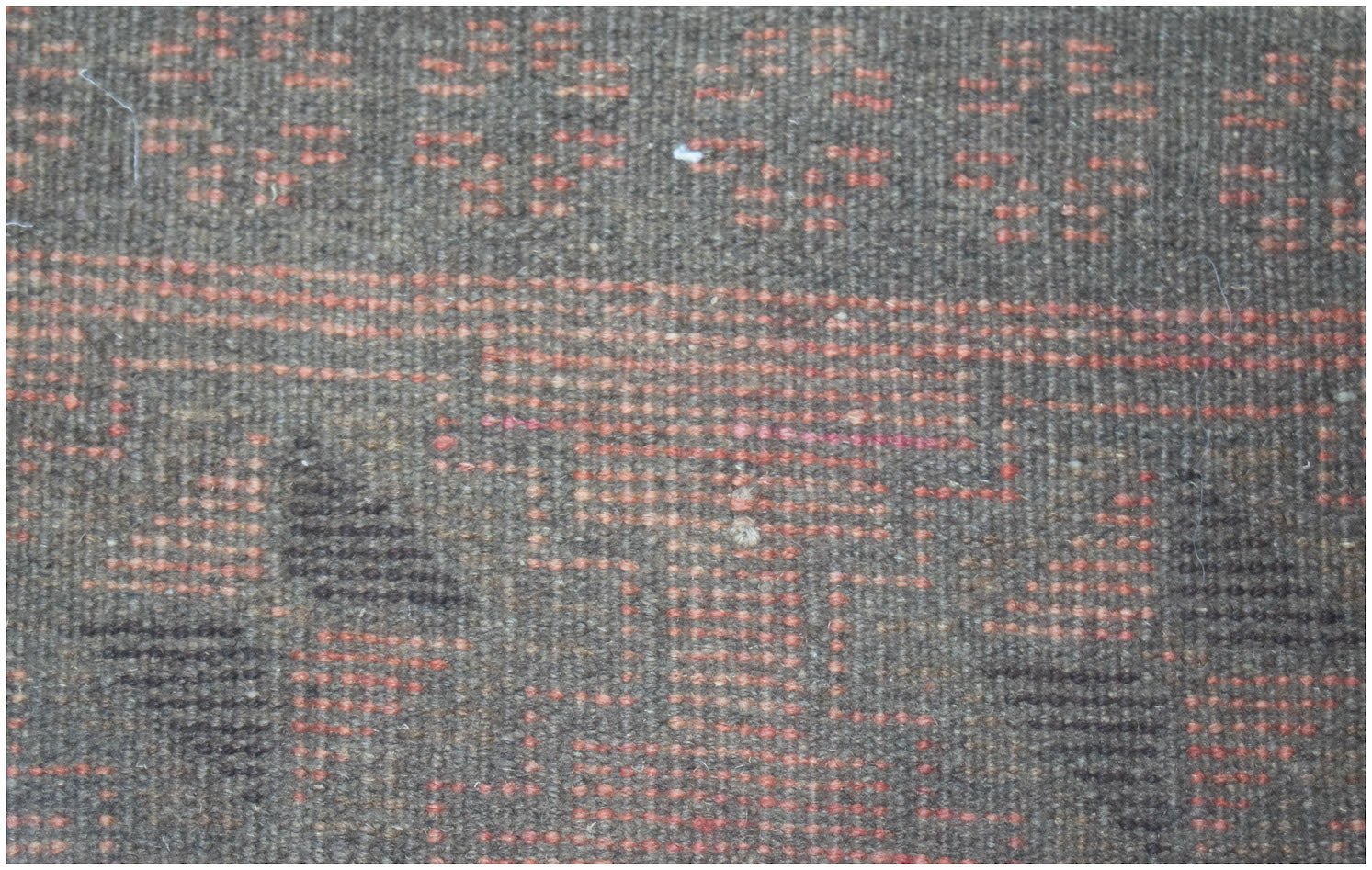 A close-up of a handmade Afghan Baluch rug featuring geometric patterns in brown and orange wool.