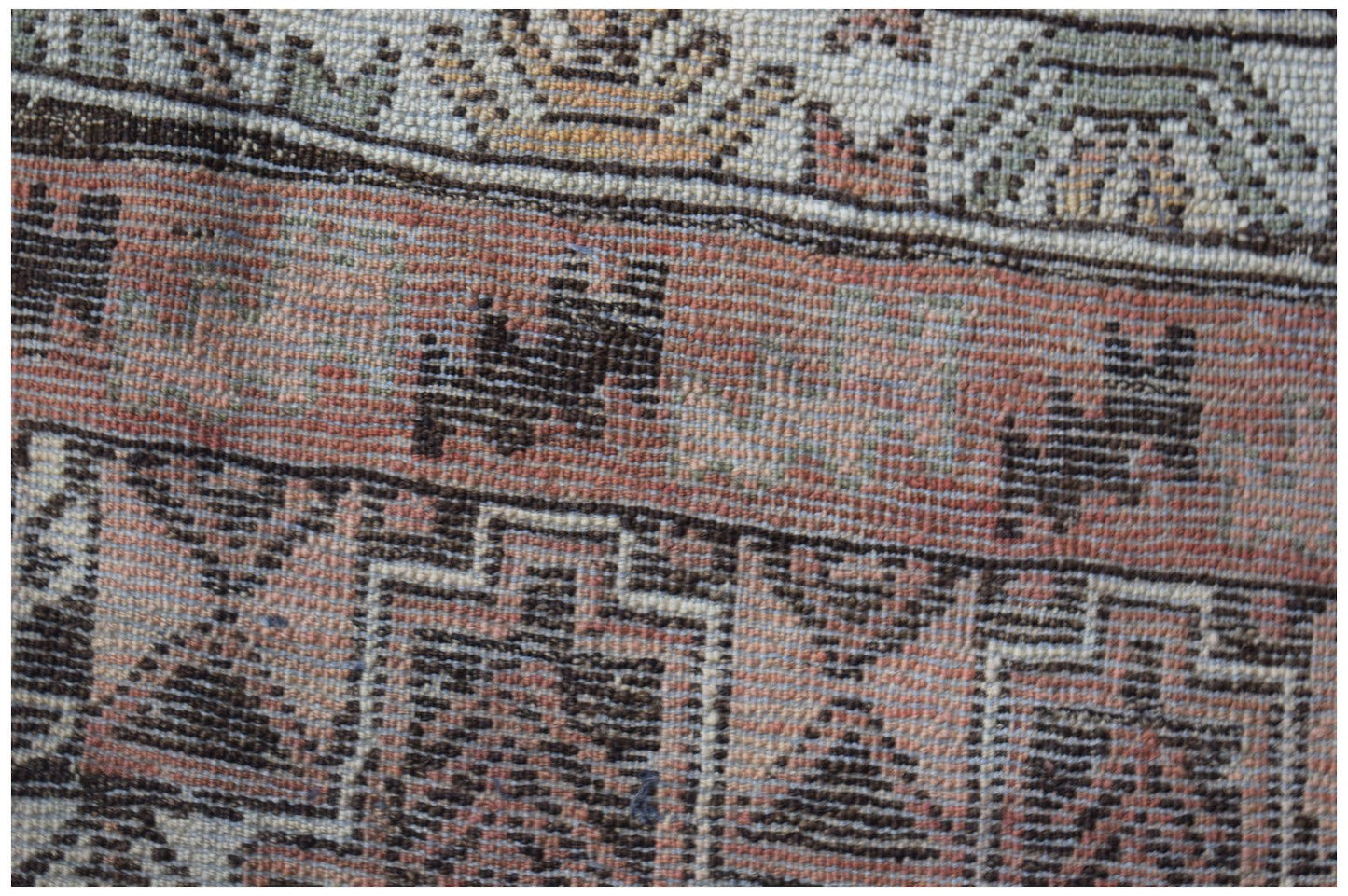 A close-up of an Afghan Baluch rug featuring geometric patterns in shades of red, brown, and cream.
