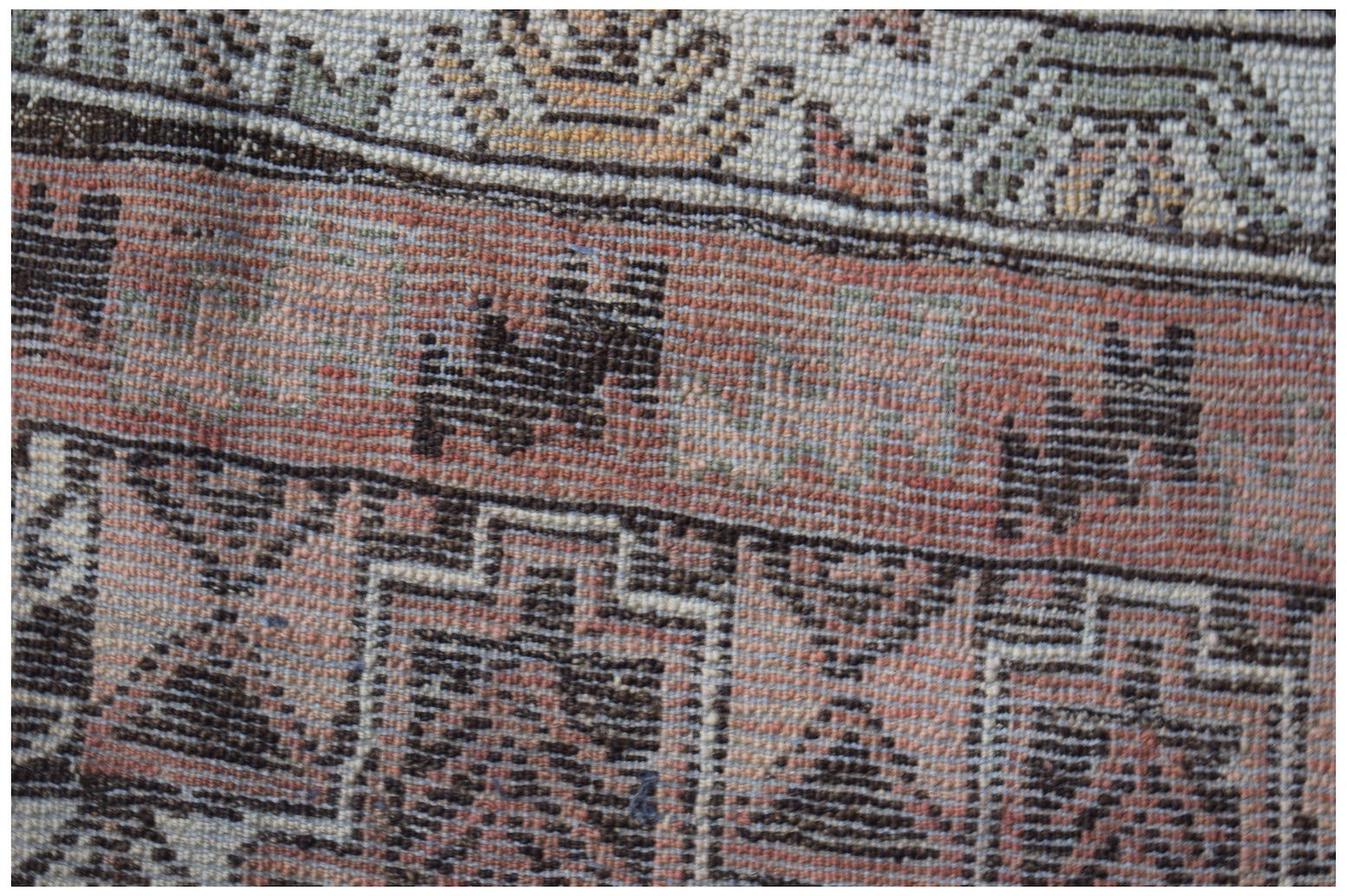 A close-up of an Afghan Baluch rug featuring geometric patterns in shades of red, brown, and cream.
