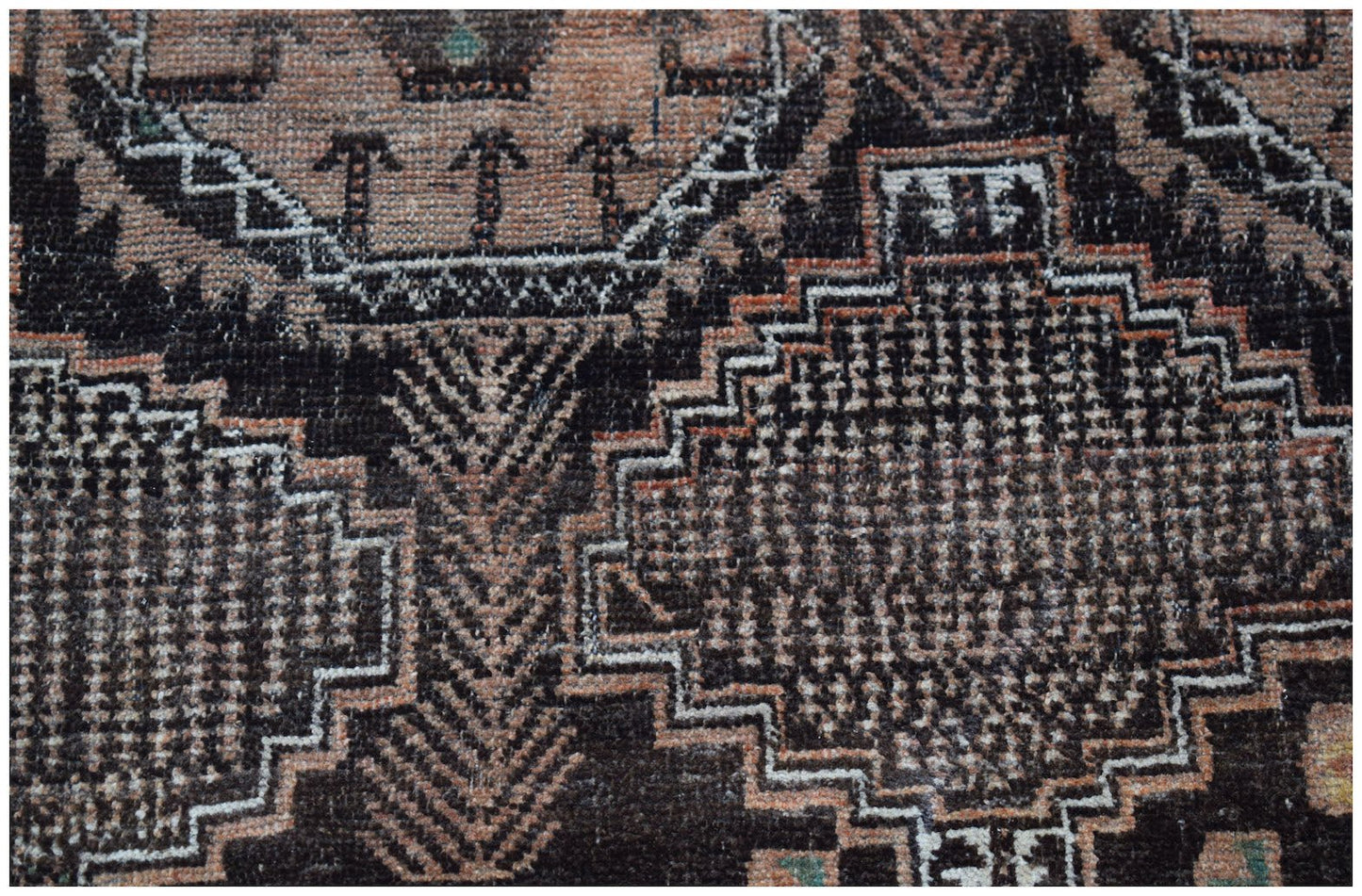 A handmade Afghan Baluch wool rug featuring intricate geometric patterns in black and muted orange.