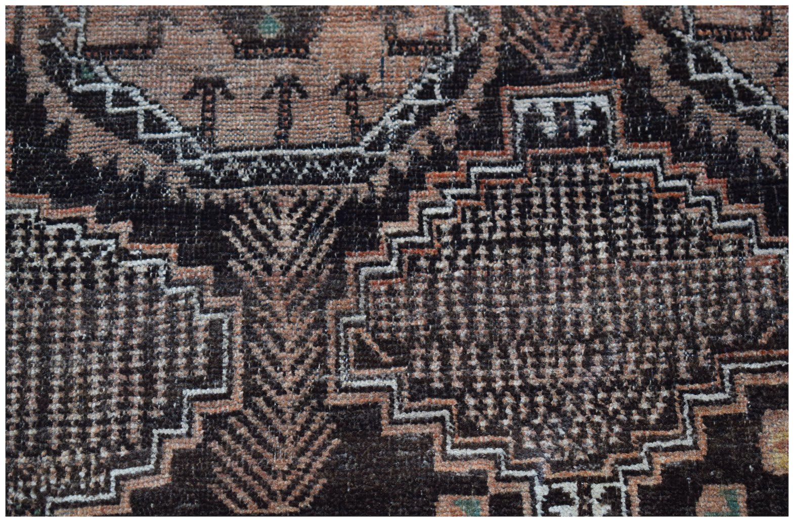 A handmade Afghan Baluch wool rug featuring intricate geometric patterns in black and muted orange.