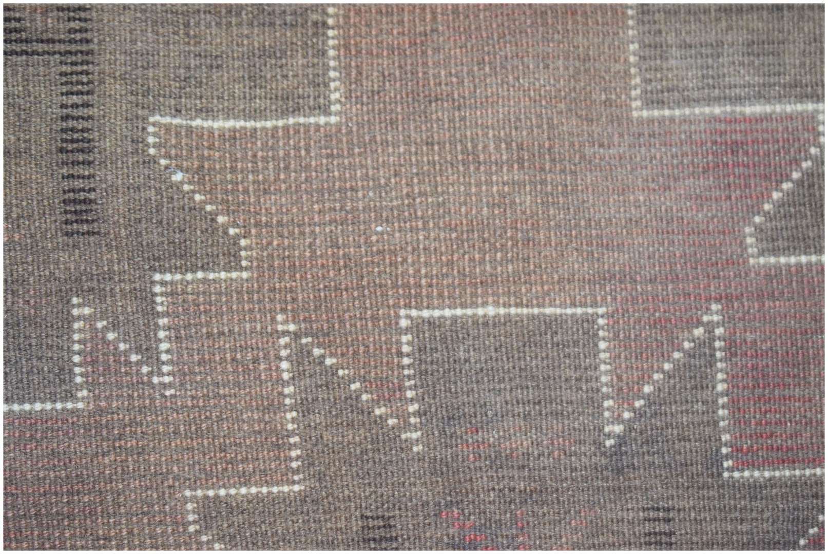 A close-up of a handmade Afghan Baluch rug featuring geometric patterns in brown and red wool.