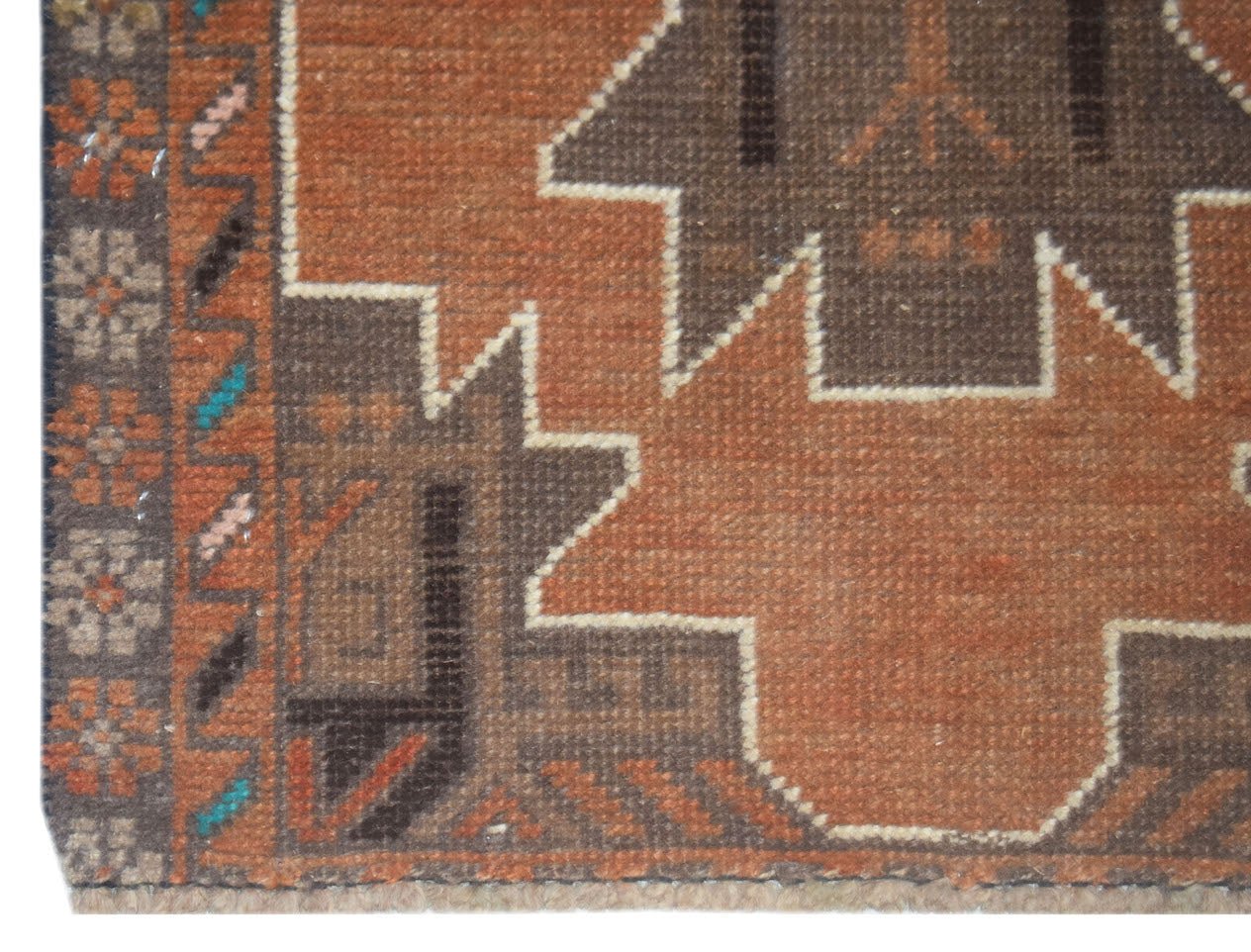A handmade Afghan Baluch rug featuring geometric patterns in shades of brown and orange.