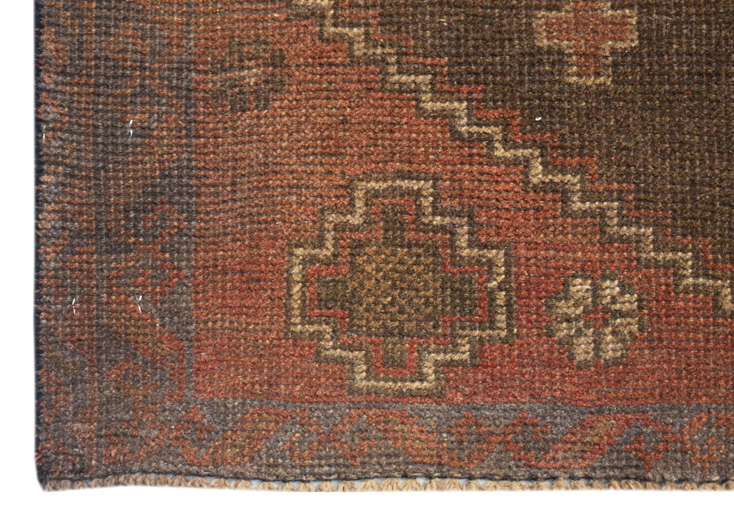 A handmade Afghan Baluch rug featuring geometric patterns in shades of brown and rust red.