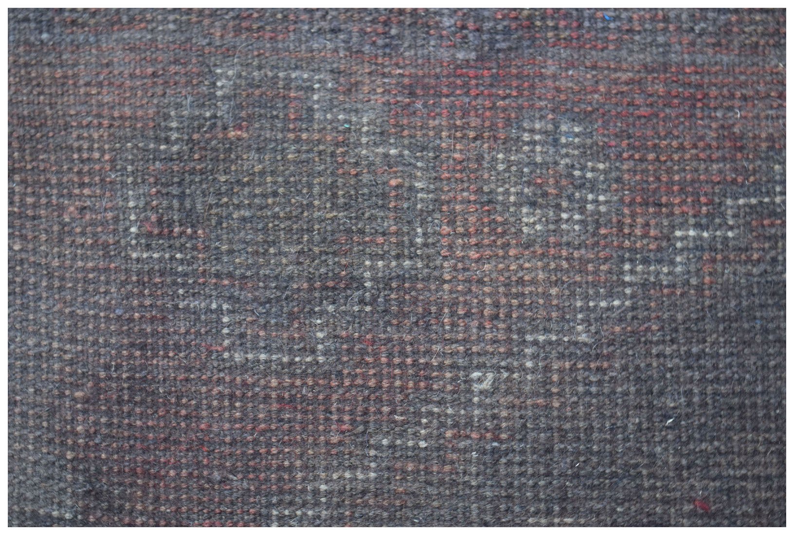 A close-up view of a handmade Afghan Baluch rug featuring a dark, geometric wool pattern.