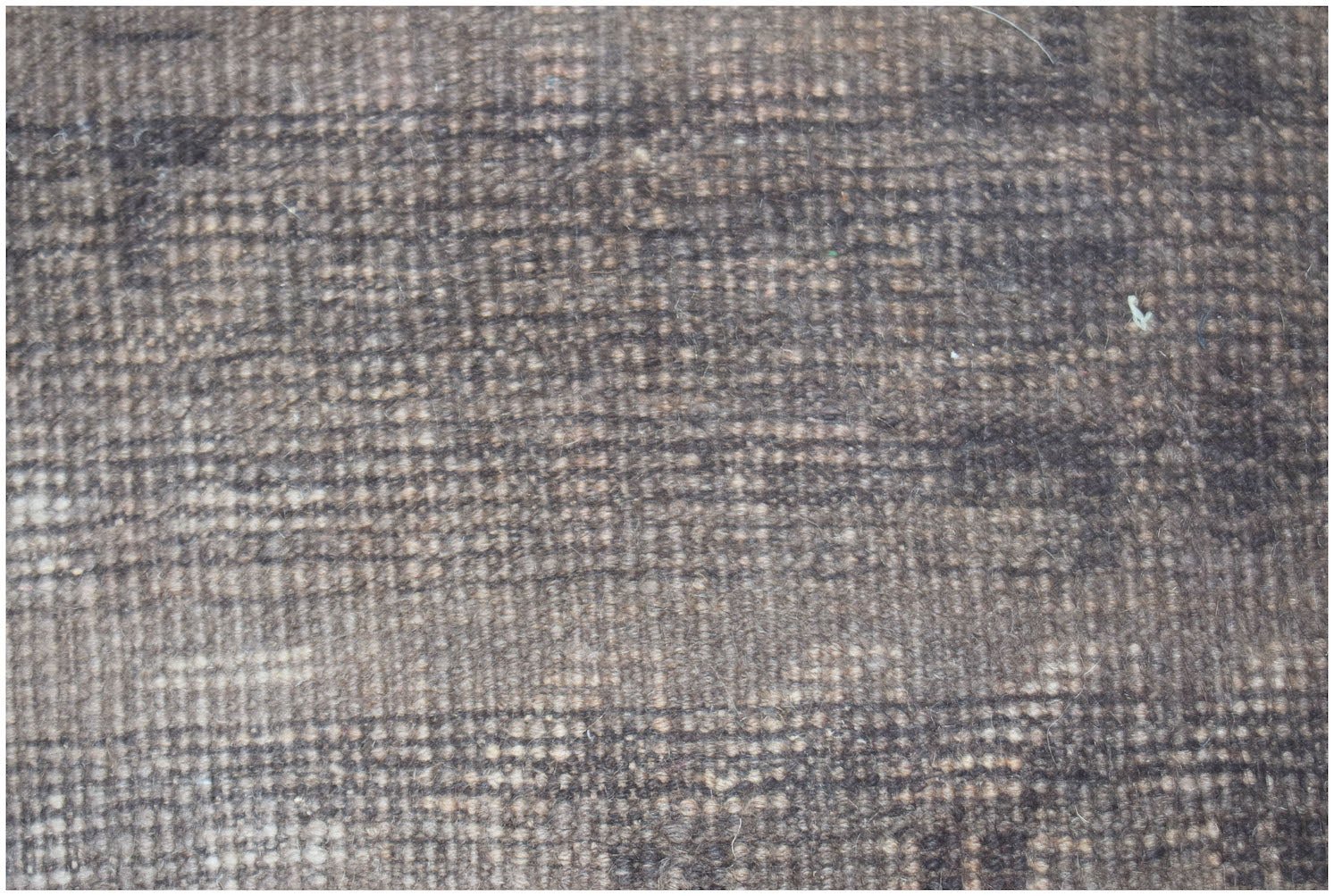 A close-up view of a handmade Afghan Baluch rug featuring a dark, textured wool pattern.