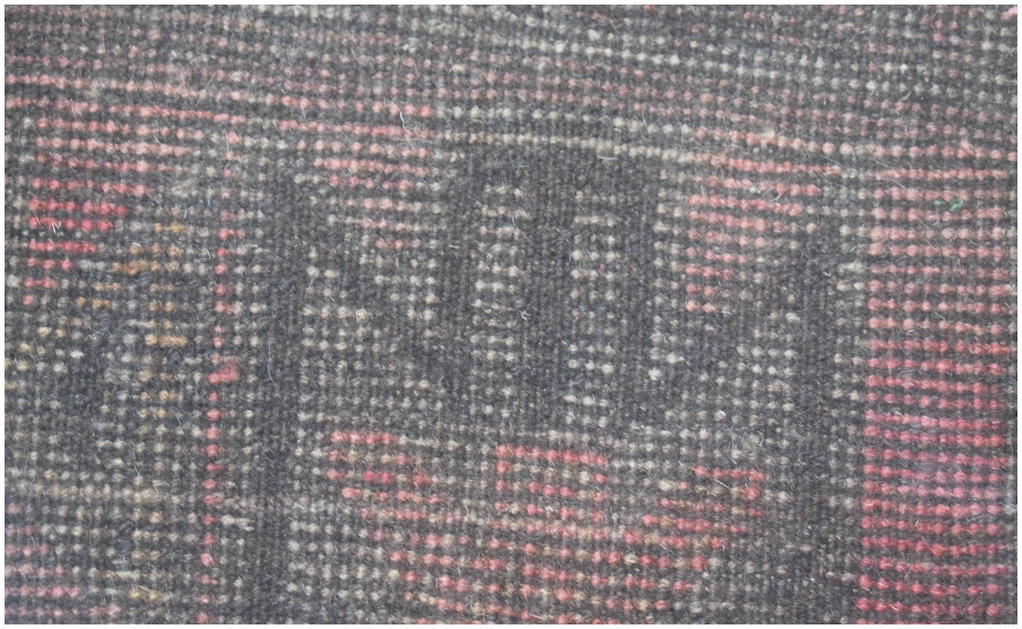A close-up of a handmade Afghan Baluch rug featuring a dark geometric pattern with red accents.