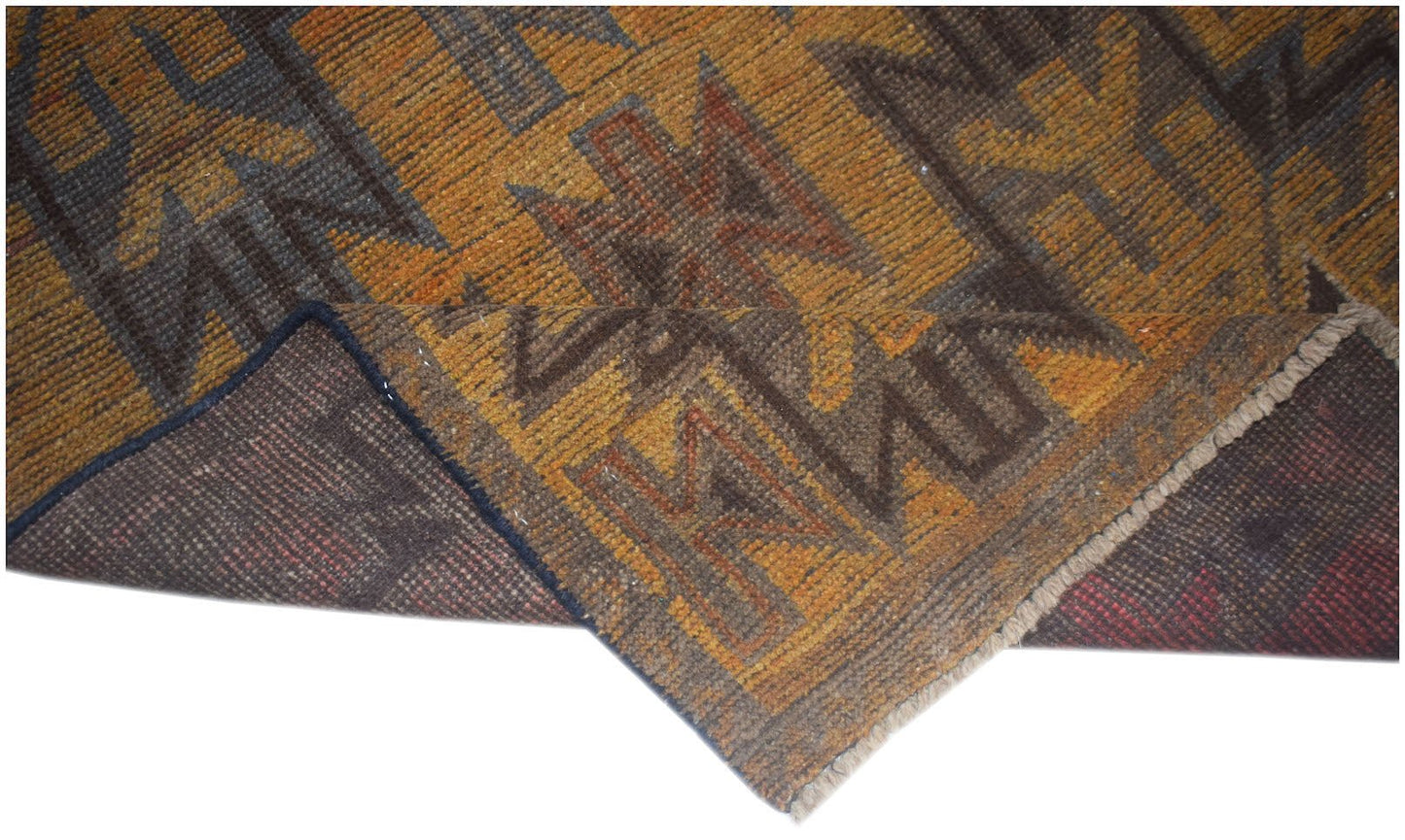A handmade Afghan Baluch rug with a geometric pattern in shades of brown, orange, and dark grey.