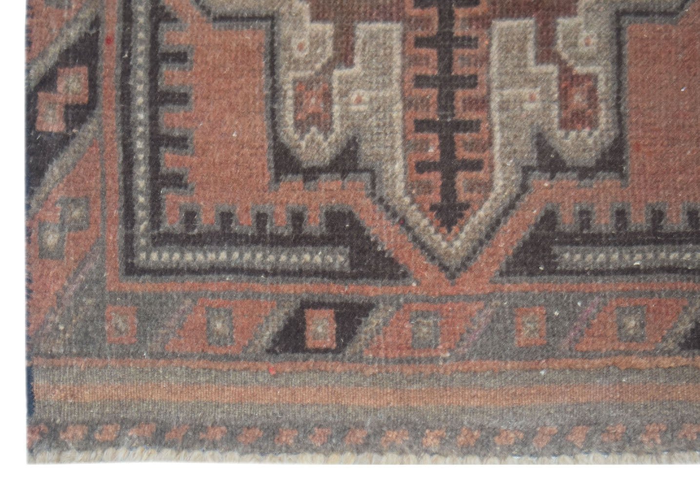 A handmade Afghan Baluch wool rug featuring geometric patterns in shades of brown and rust.