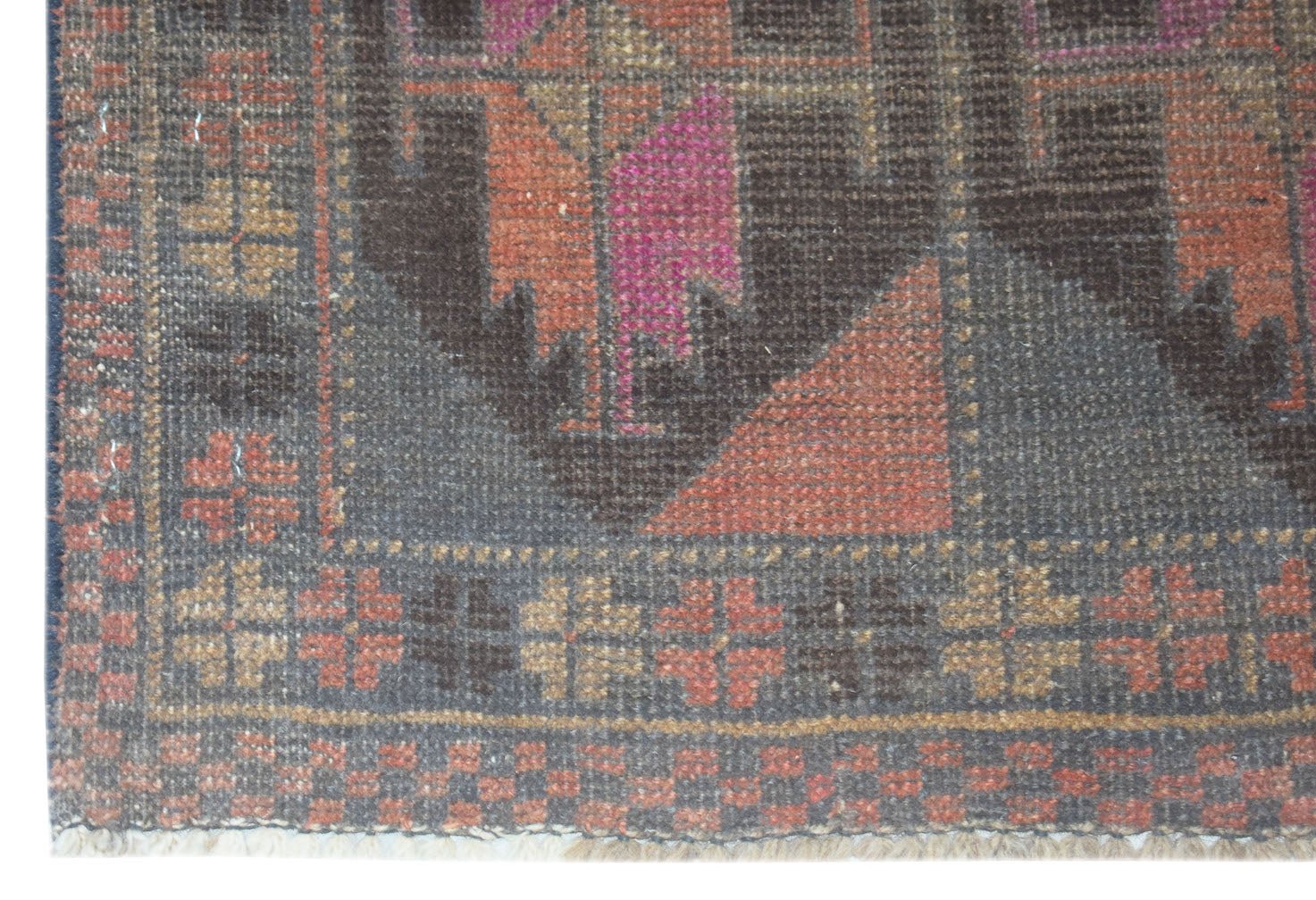 A handmade Afghan Baluch rug featuring geometric patterns in shades of charcoal, red, and pink.
