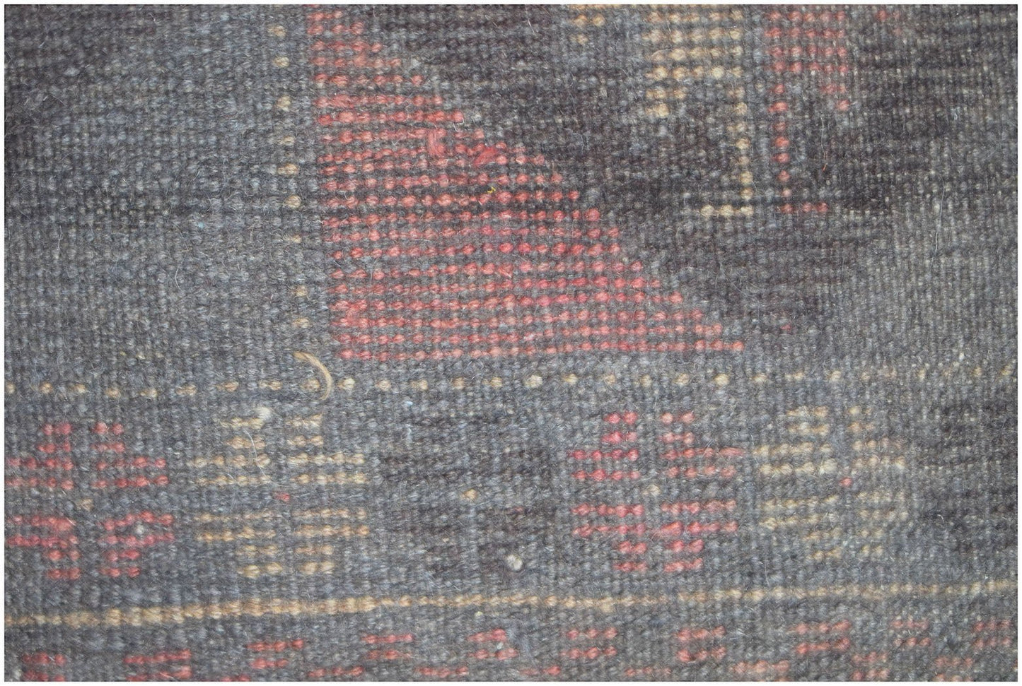 A close-up view of a handmade Afghan Baluch rug featuring geometric patterns in red and tan wool.