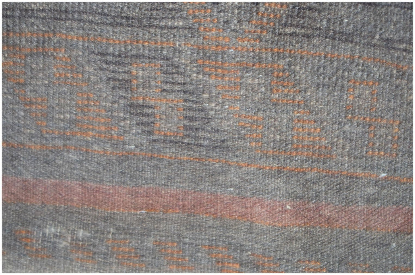 A close-up of a handmade Afghan Baluch rug featuring geometric orange patterns on a dark wool base.