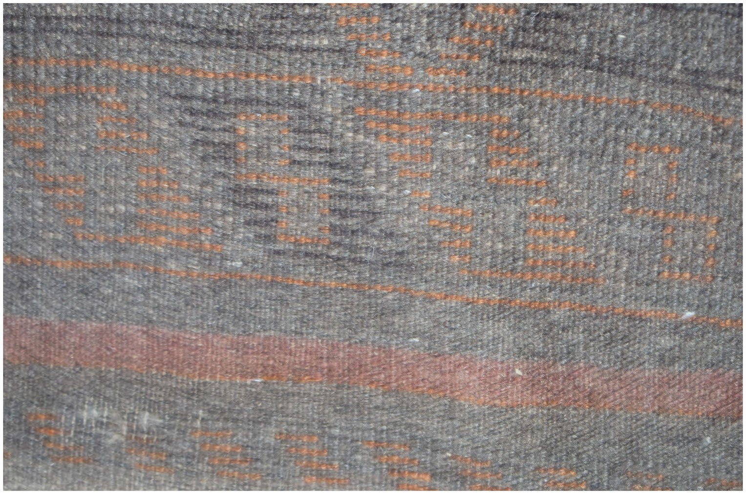 A close-up of a handmade Afghan Baluch rug featuring geometric orange patterns on a dark wool base.