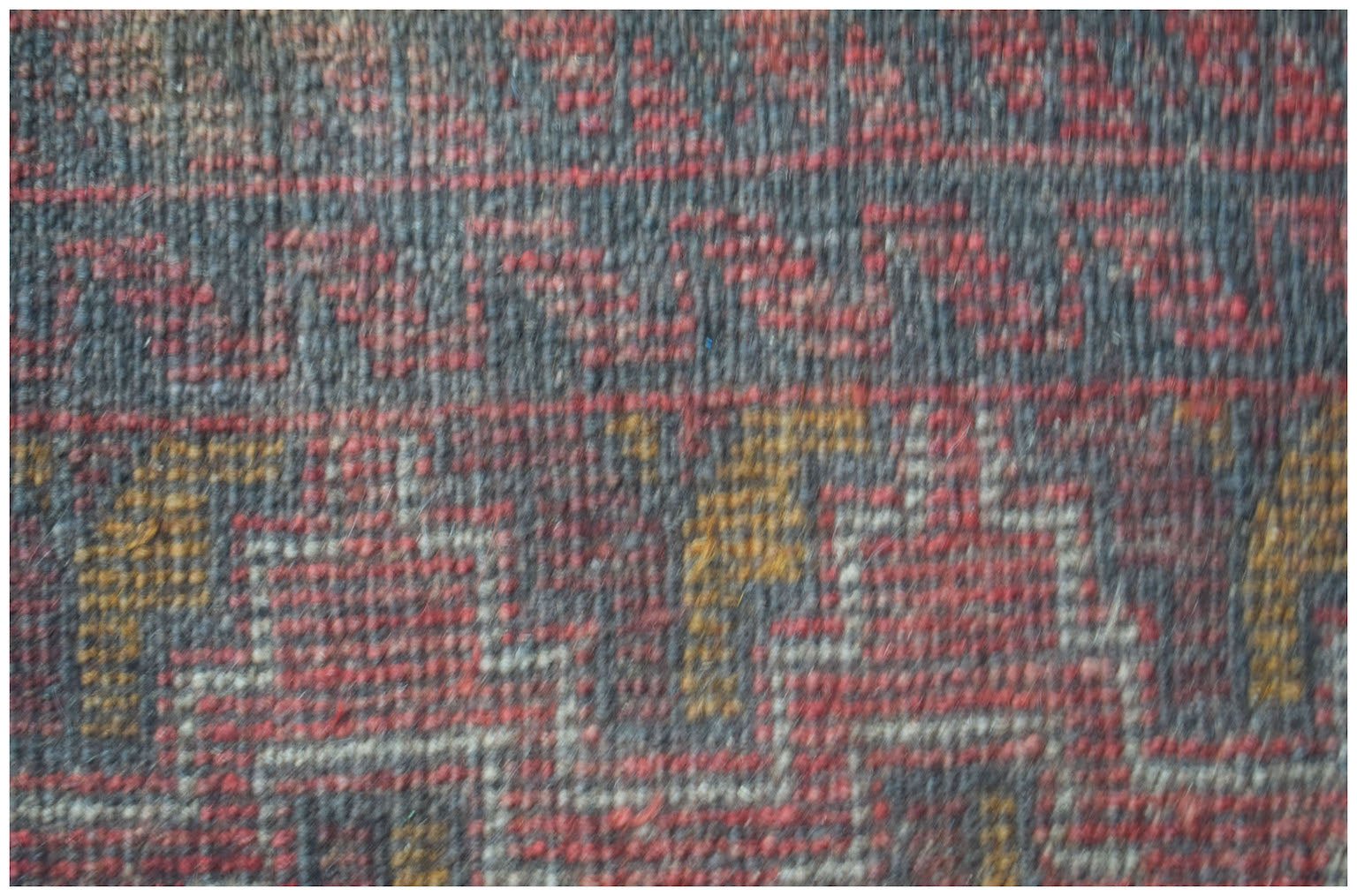 A close-up view of a handmade Afghan Baluch rug featuring geometric patterns in red, gold, and grey.