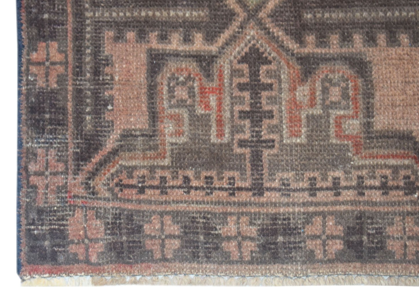 A close-up of a handmade Afghan Baluch rug featuring geometric patterns in brown and muted red.