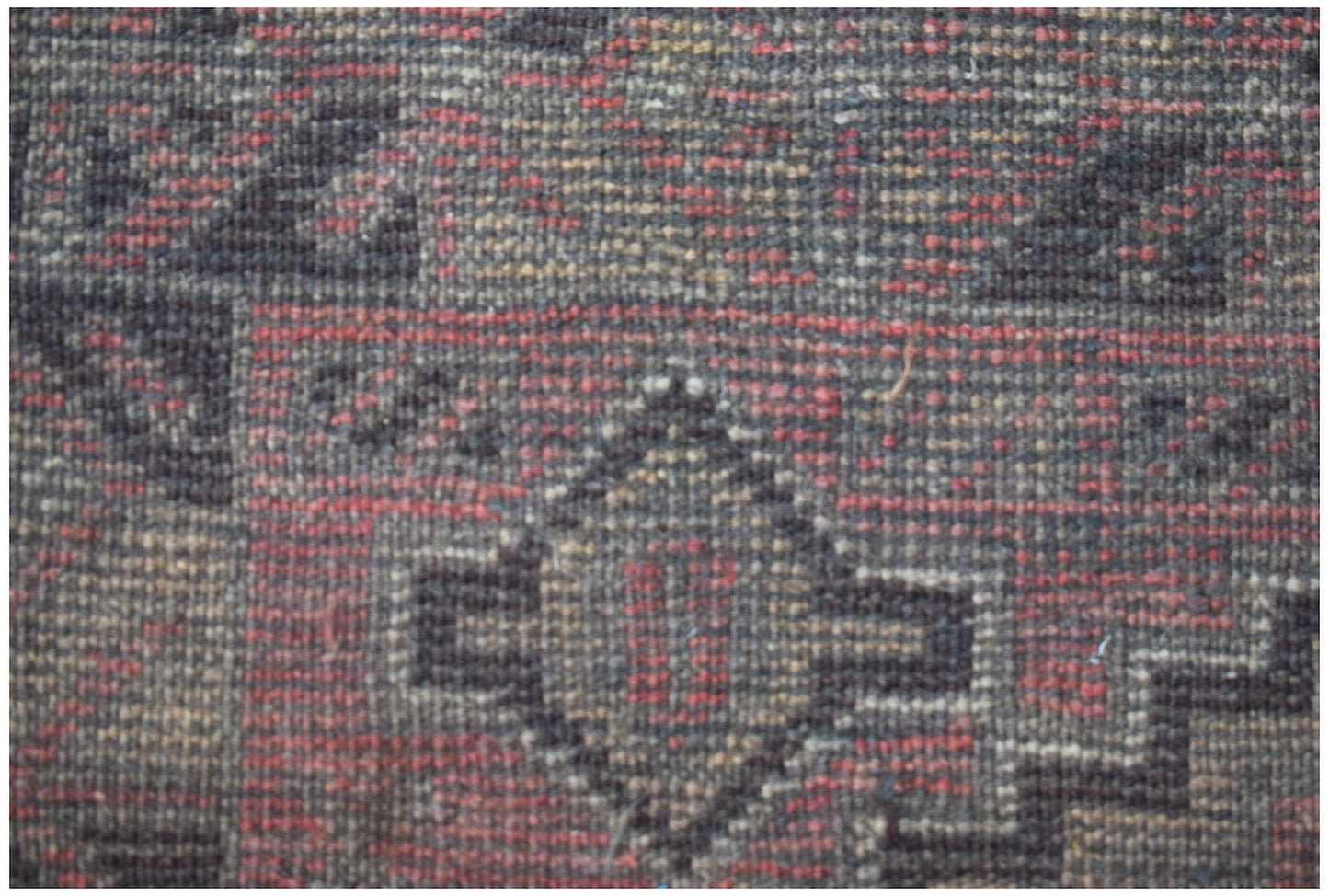 A close-up of a handmade Afghan Baluch rug featuring geometric diamond patterns in red and black.