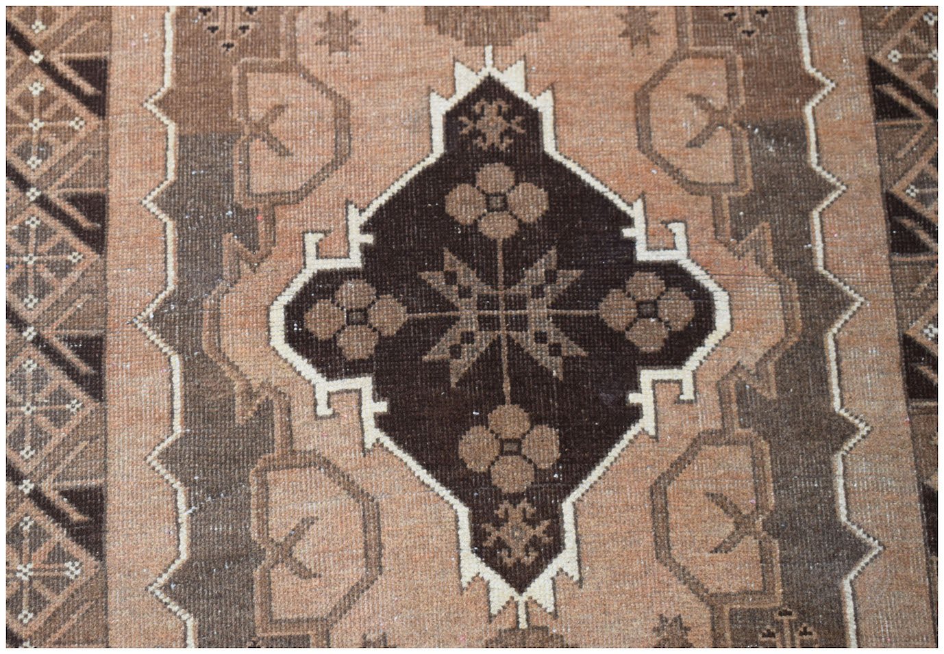 Handmade Afghan Baluch rug featuring a dark brown central medallion with floral motifs on tan wool.