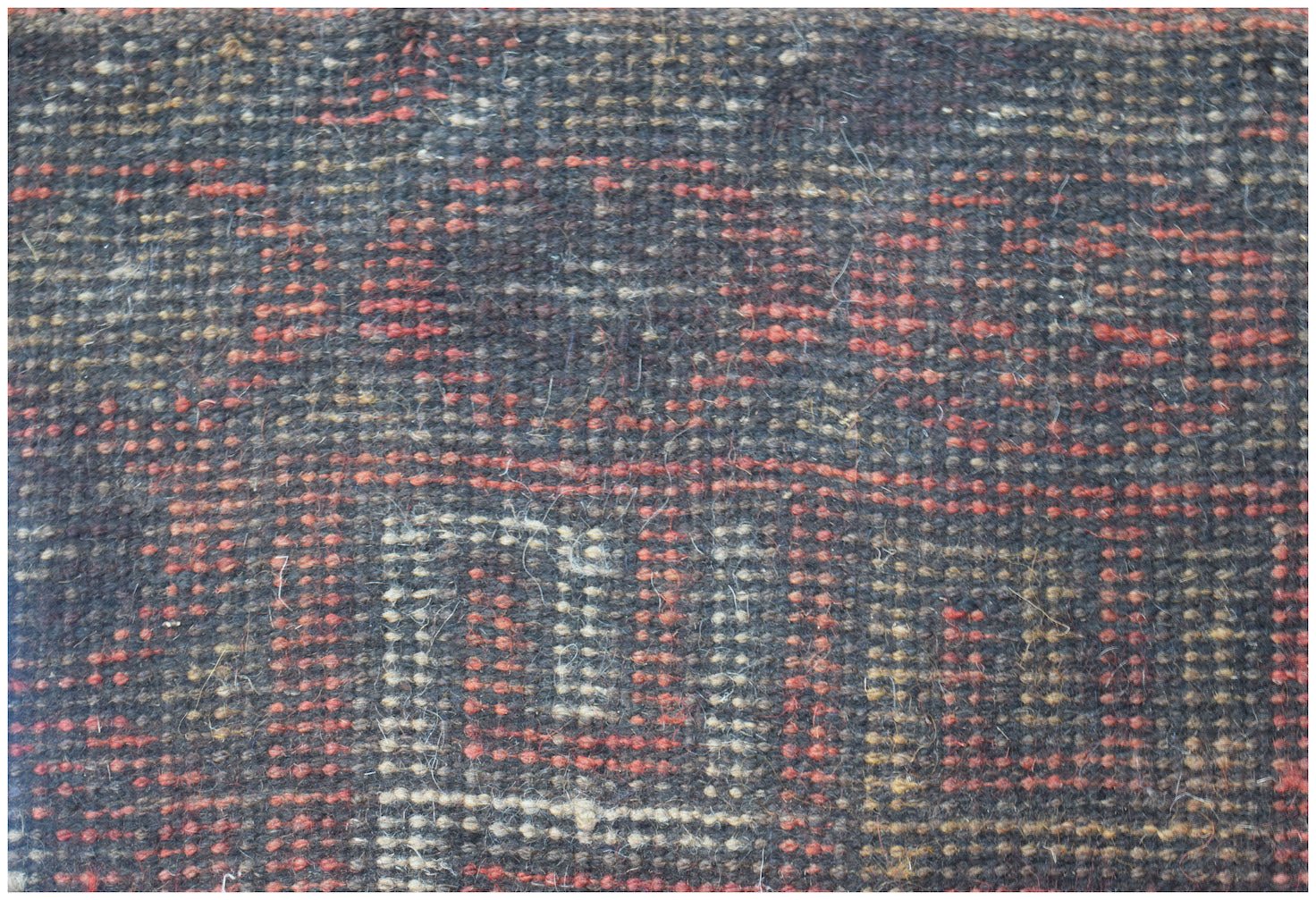 A close-up of a handmade Afghan Baluch rug featuring a geometric pattern in red, black, and tan.