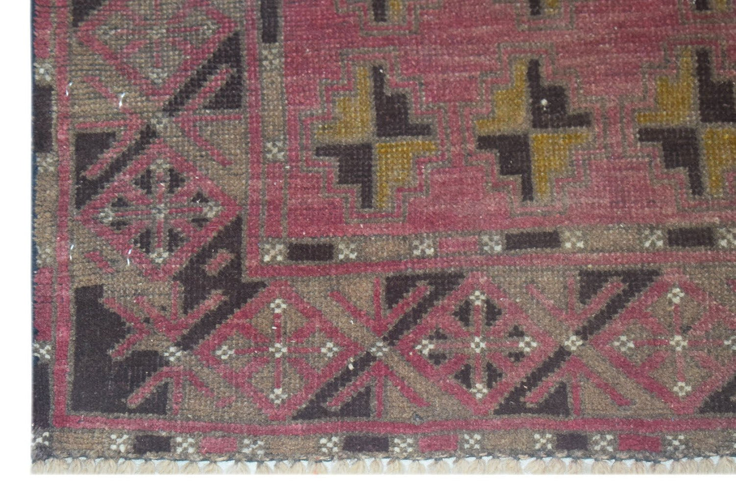 A handmade Afghan Baluch rug featuring geometric patterns in shades of pink, brown, and gold.