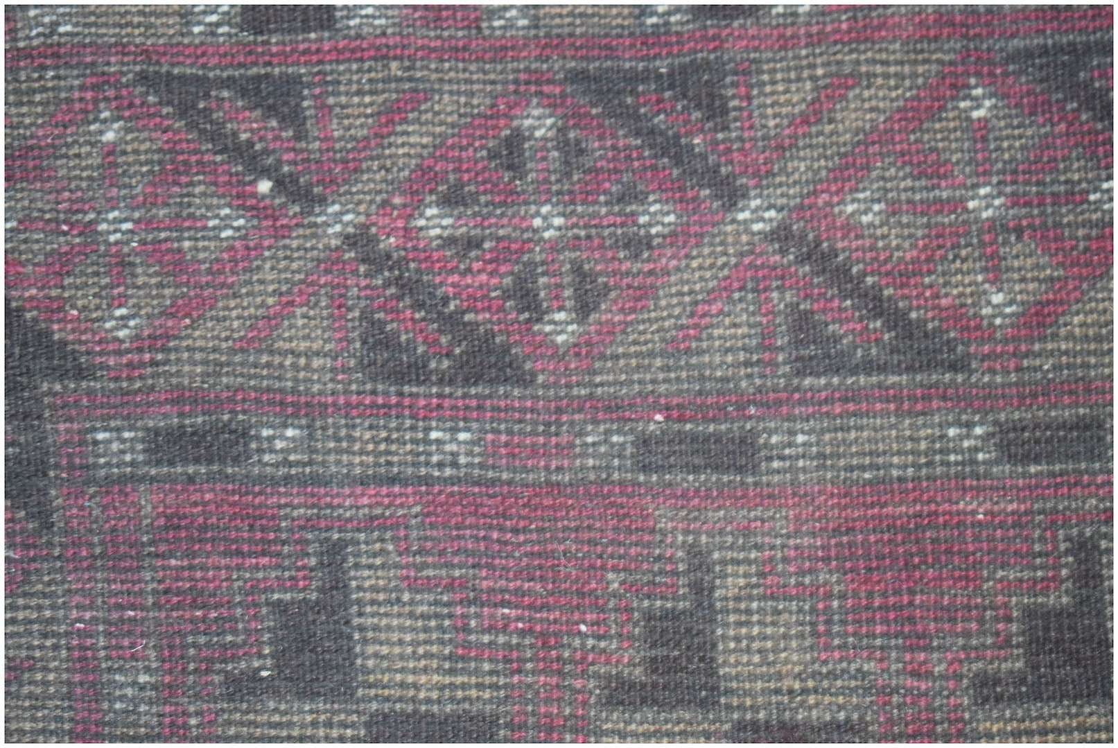 A close-up of a handmade Afghan Baluch rug featuring geometric diamond and step patterns in wool.