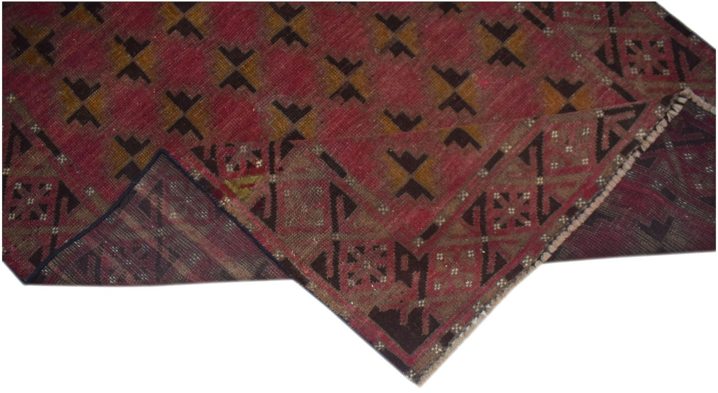 A handmade Afghan Baluch rug featuring a red field with geometric patterns and a dark border.