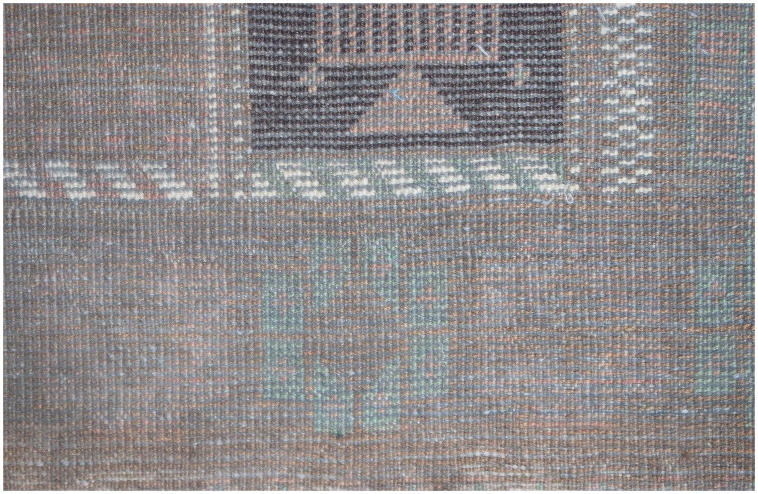 A close-up of a handmade Afghan Baluch rug featuring geometric patterns in brown and muted green.