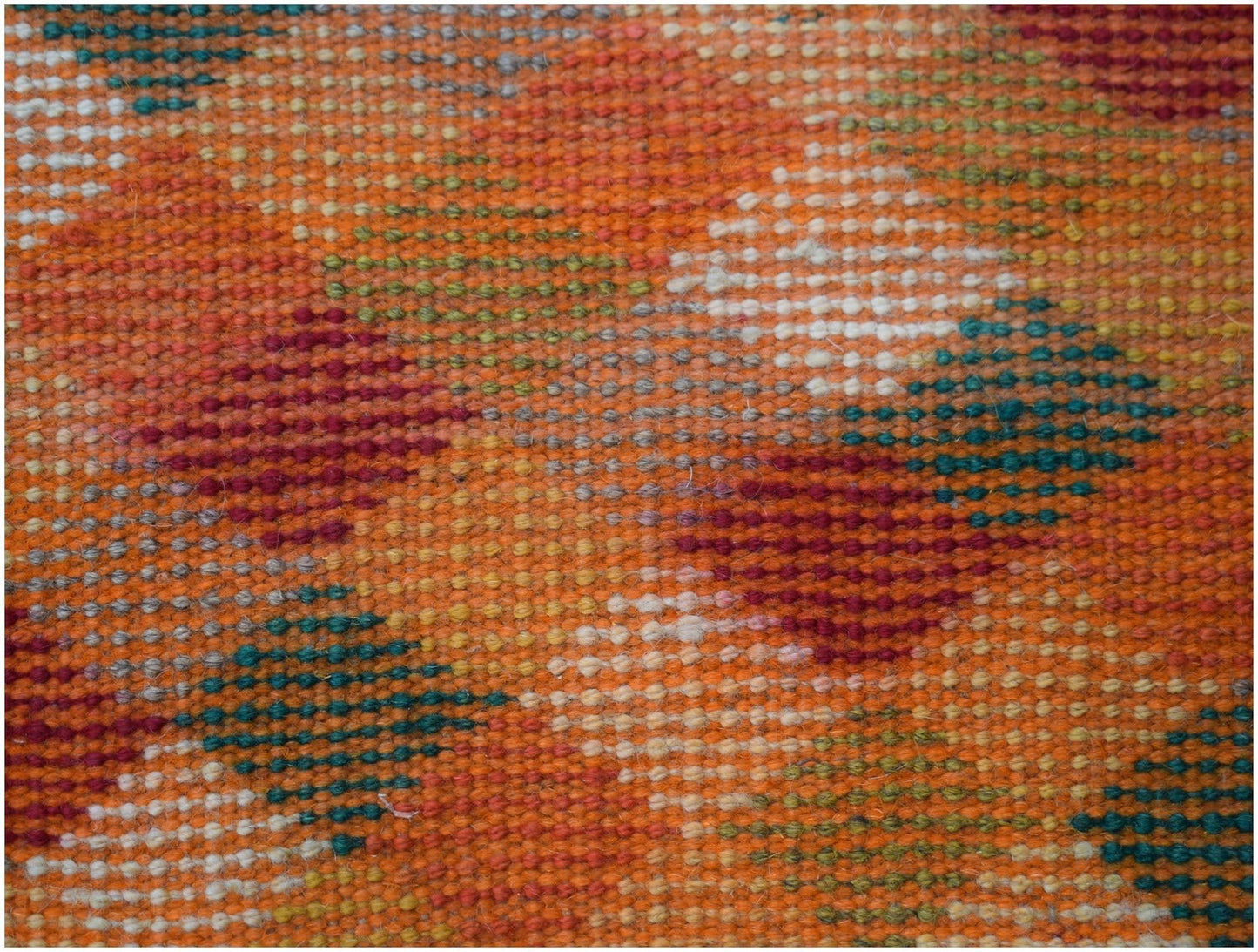 A handmade Afghan Baluch wool rug featuring a geometric pattern in orange, red, blue, and ivory.