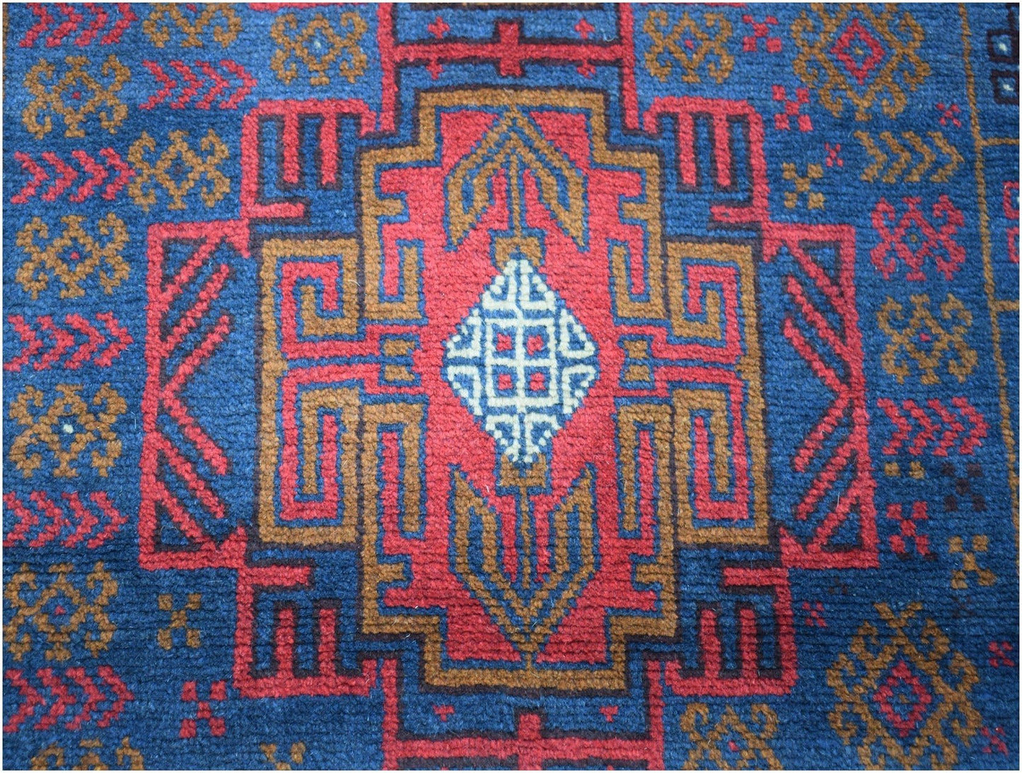 Handmade Afghan Baluch rug featuring a geometric tribal pattern in red, blue, and brown wool.