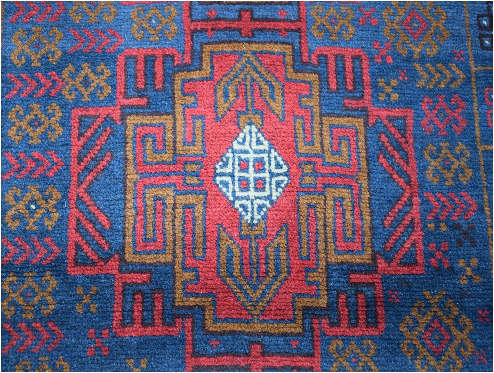 Handmade Afghan Baluch rug featuring a geometric tribal pattern in red, blue, and brown wool.