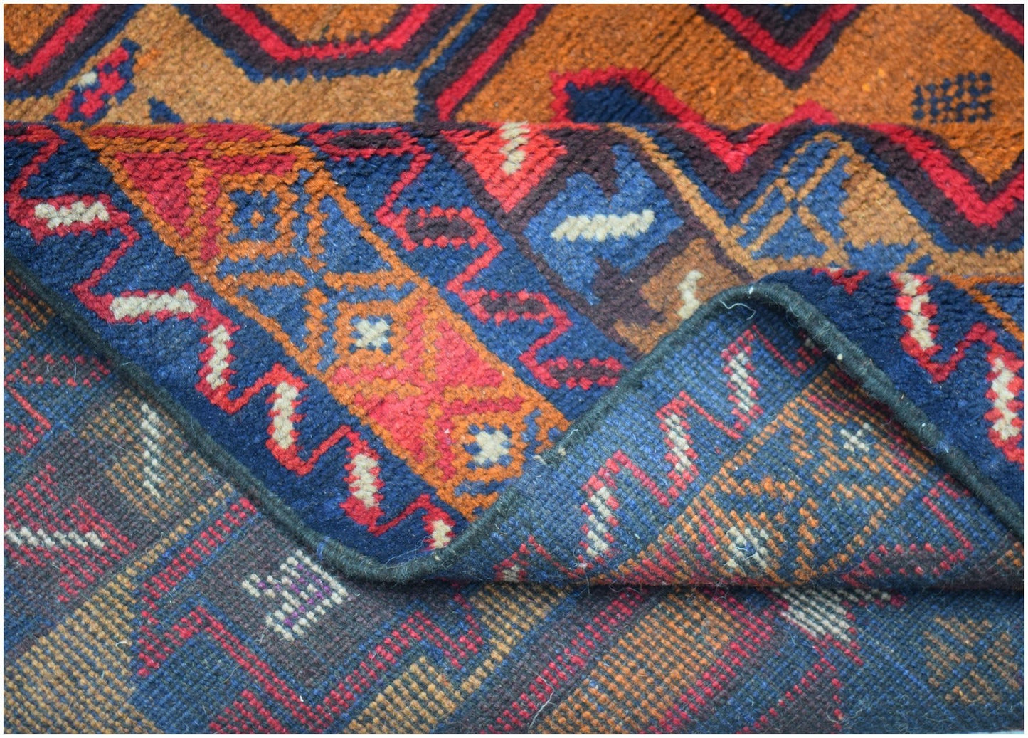 A handmade Afghan Baluch rug featuring geometric patterns in deep red, blue, and brown wool.