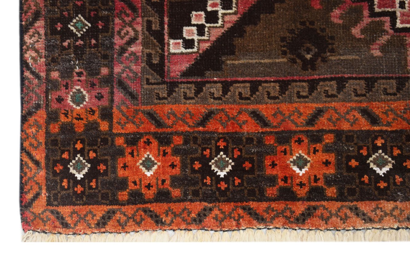 A handmade Afghan Baluch rug featuring geometric patterns in shades of red, brown, and black.