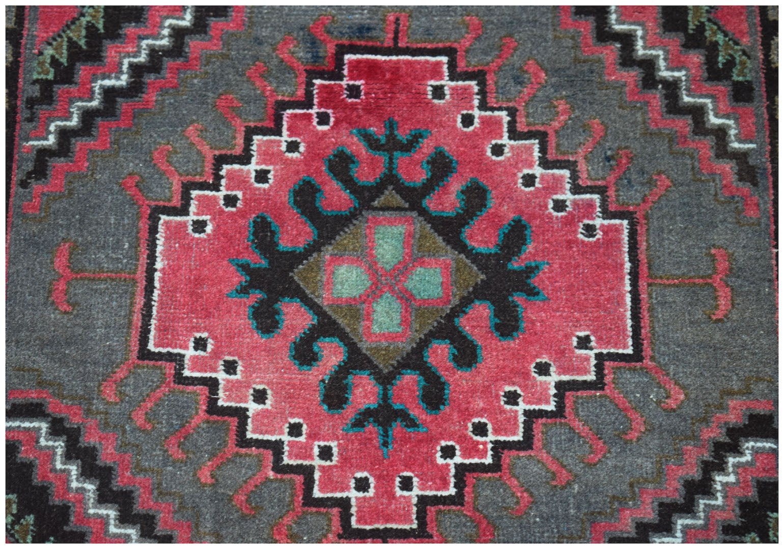 Handmade Afghan Baluch rug featuring a central geometric diamond motif in pink, black, and teal.