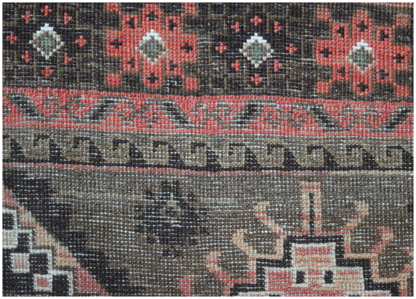 A close-up of an Afghan Baluch rug featuring geometric floral motifs and traditional border patterns.