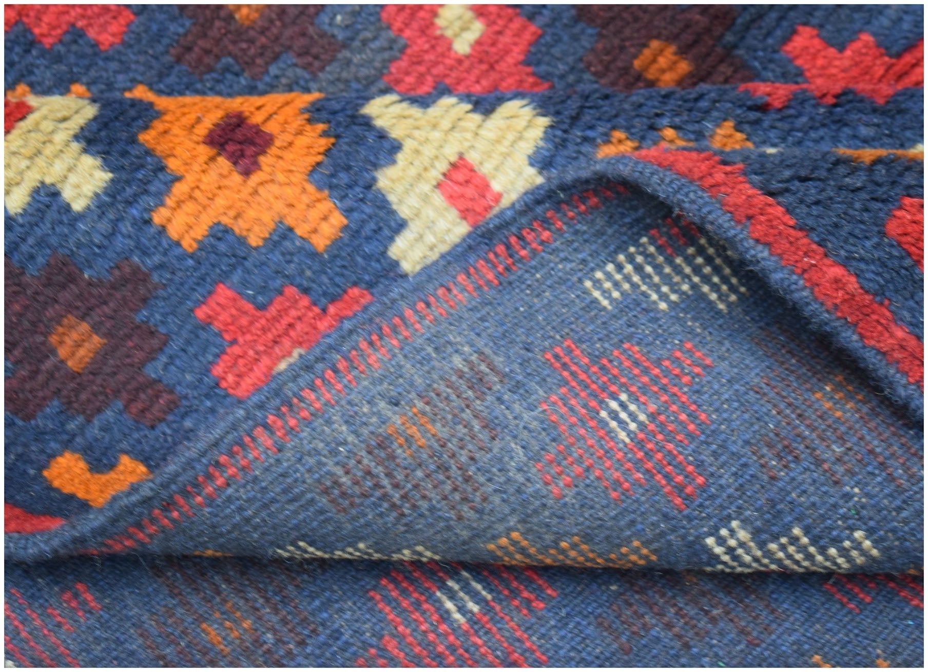 A handmade Afghan Baluch rug featuring a geometric pattern in dark blue, red, and ivory wool.