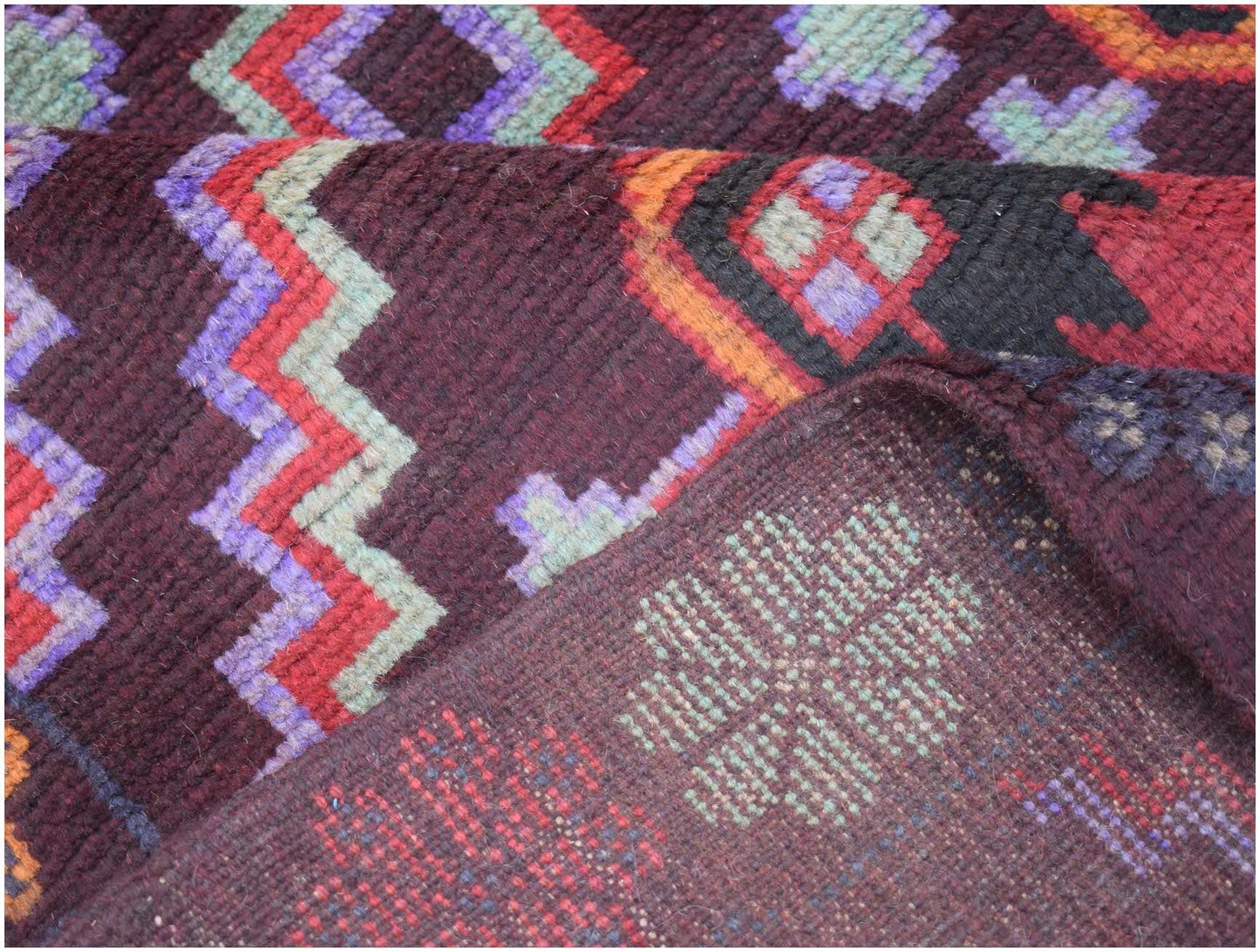 A handmade Afghan Pashm rug featuring geometric zigzag patterns in deep red, blue, and ivory.